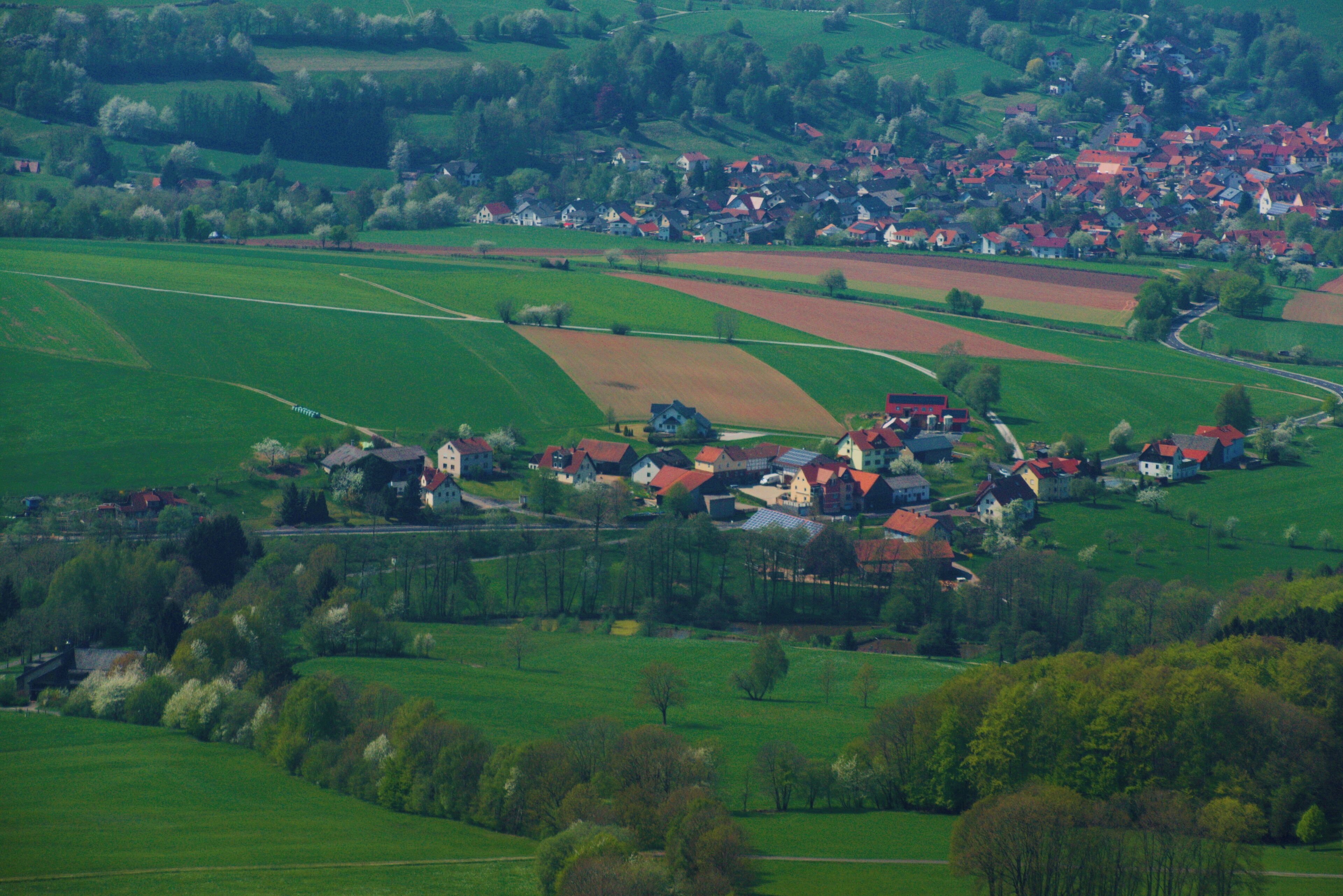 A rural landscape with rolling green fields, scattered houses, and a small village.