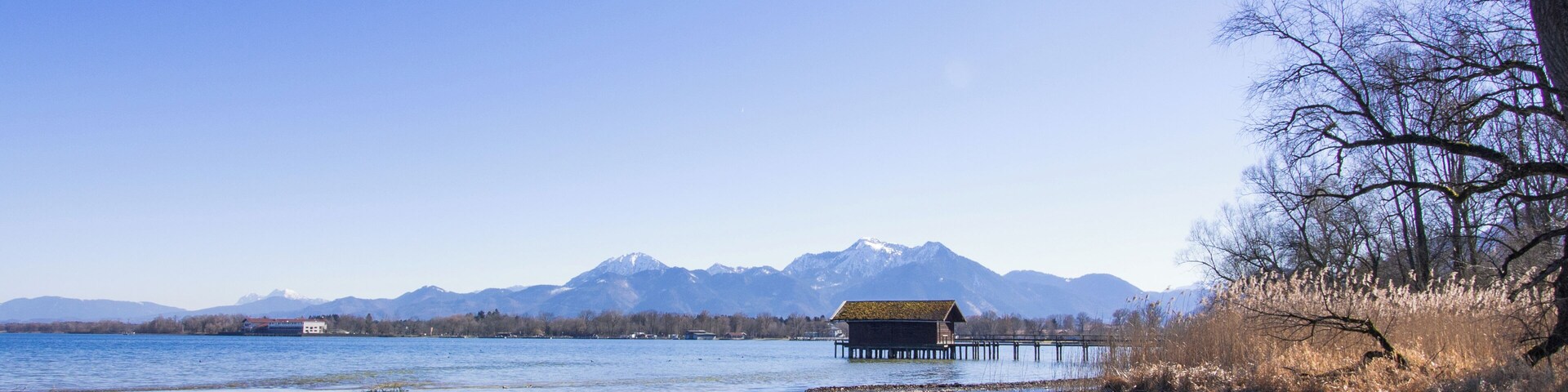 Un lago tranquilo con un muelle de madera, una casa en la orilla y montañas al fondo.