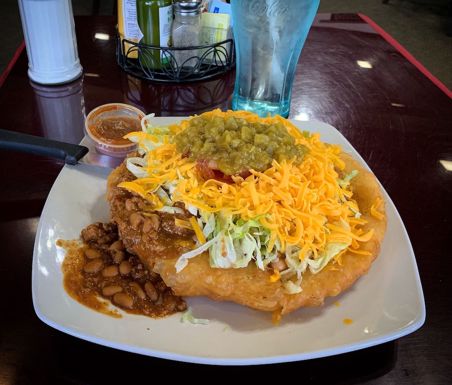 Un plato de comida con un alimento frito cubierto de queso rallado, frijoles y salsa verde.
