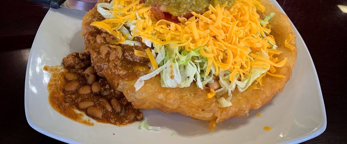 A plate of food with a fried item topped with shredded cheese, beans, and a green sauce.
