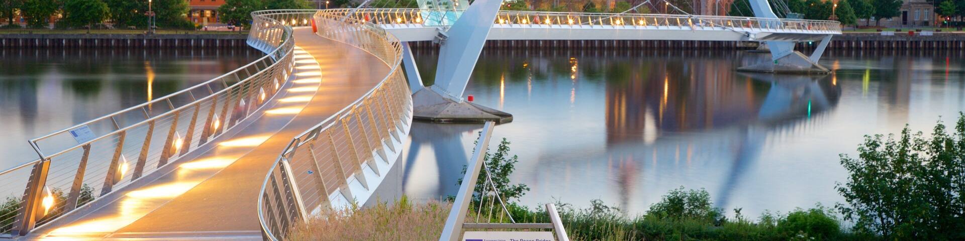 A modern bridge over a river with a cityscape in the background, including a prominent clock tower.