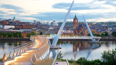 Un puente moderno sobre un río, con un paisaje urbano al fondo que destaca una torre del reloj.