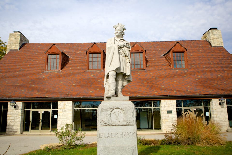 A statue in front of a building with a red-tiled roof and stone walls.