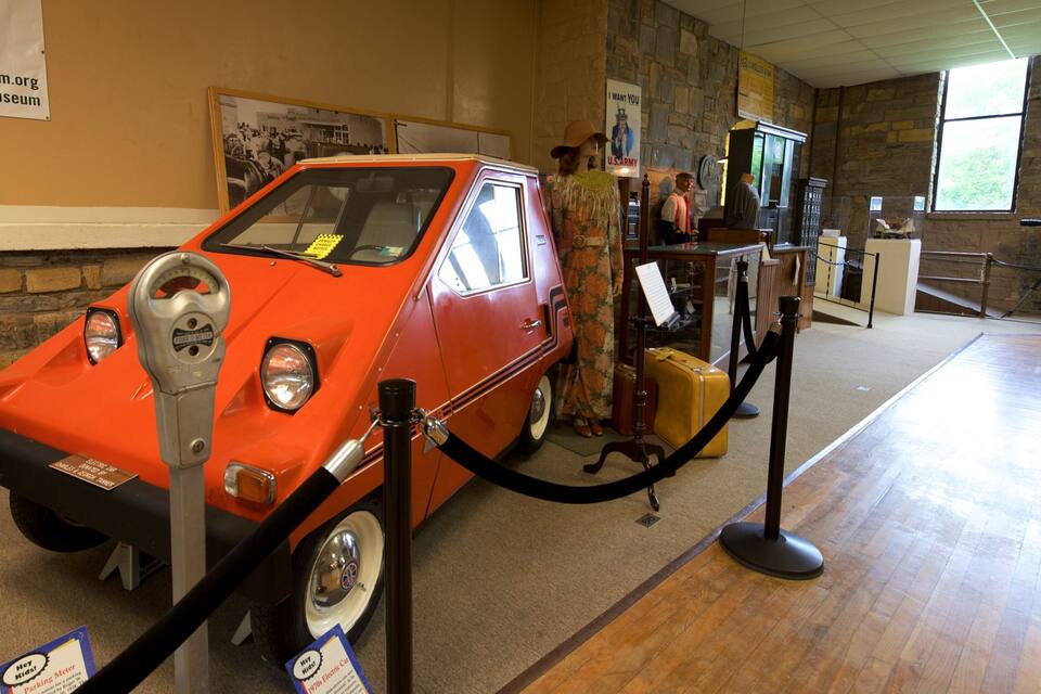 A vintage orange car on display with a parking meter in front.
