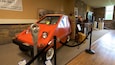 Un'auto arancione d'epoca esposta, con un parcometro di fronte.