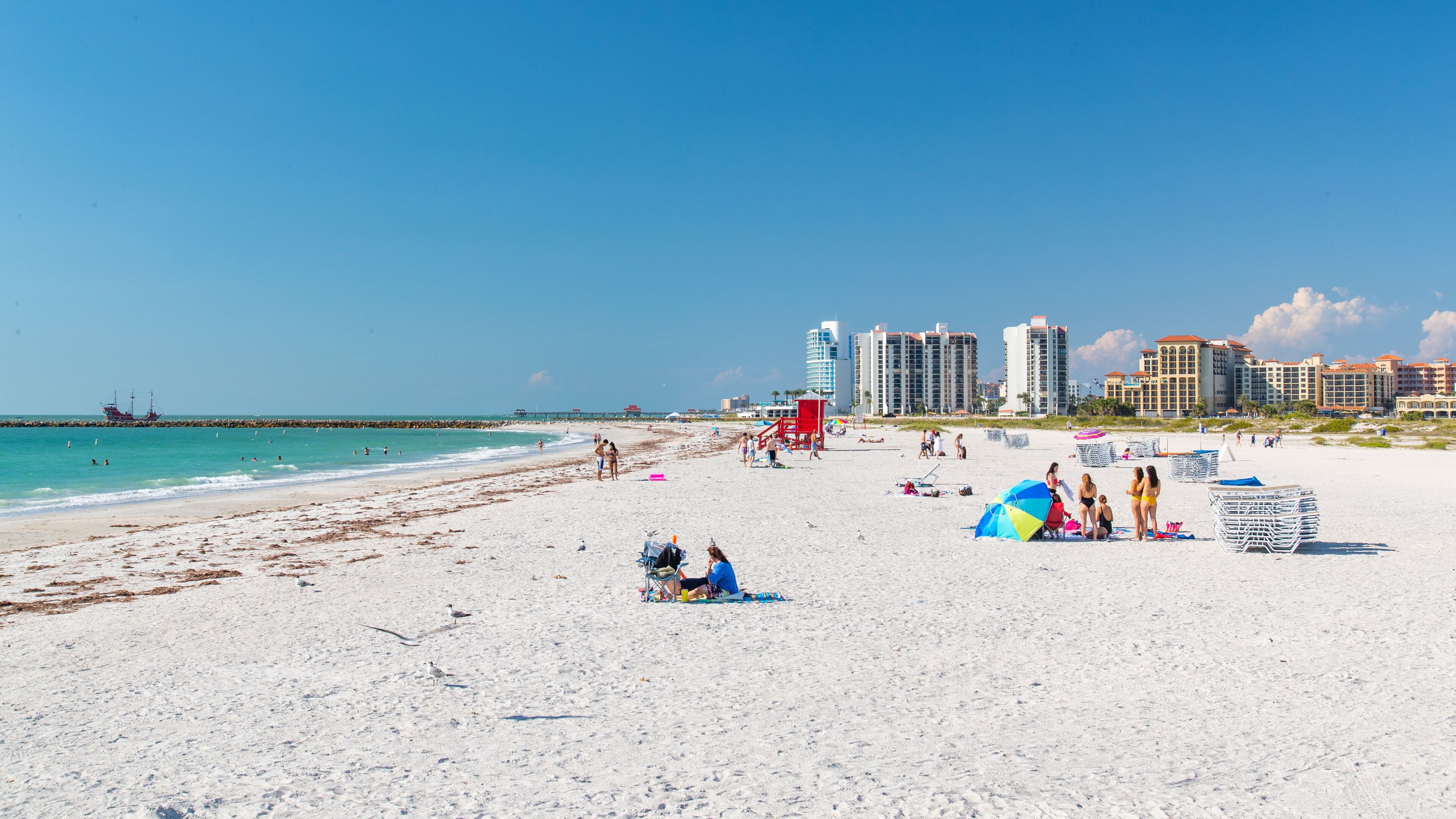Una playa de arena blanca, una torre de salvavidas y edificios altos al fondo.