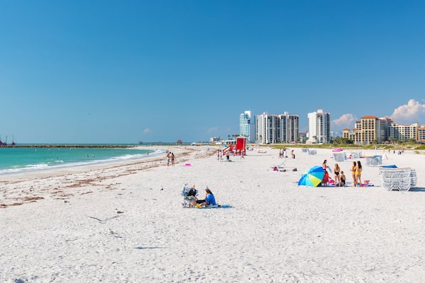 A beach with white sand, a lifeguard tower, and tall buildings in the background.