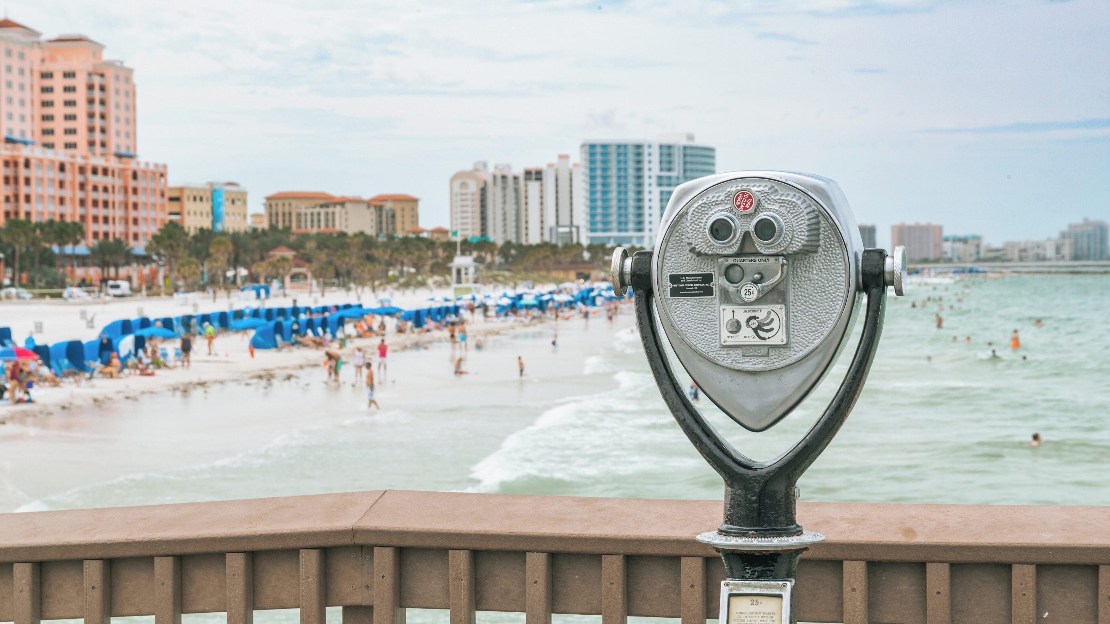 View of Clearwater Beach from Pier 60 Park featuring a coin-operated binocular viewer near the shoreline and beachgoers under umbrellas