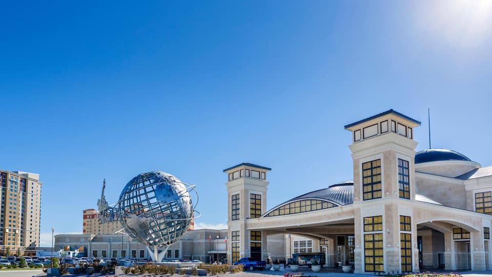 A modern building with a large glass dome and a spherical sculpture in front.