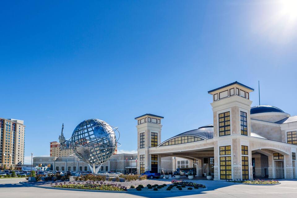 A modern building with a large glass dome and a spherical sculpture in front.