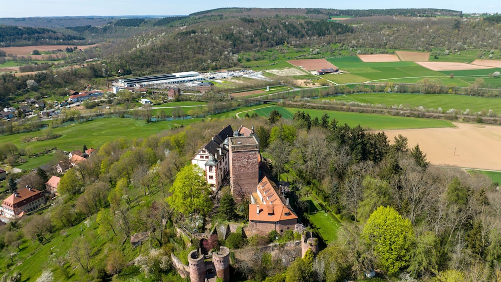 Eine Burg, umgeben von grünen Feldern und einem modernen Gebäudekomplex.