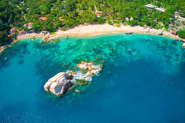 Eine Küstenlandschaft mit klarem türkisblauem Wasser, einem Sandstrand und einem Felsen.