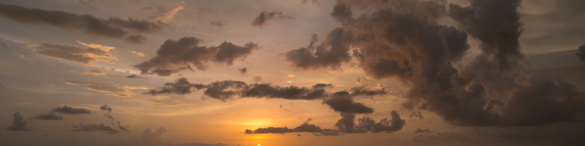 Un atardecer sobre una playa con olas y cielo nublado.