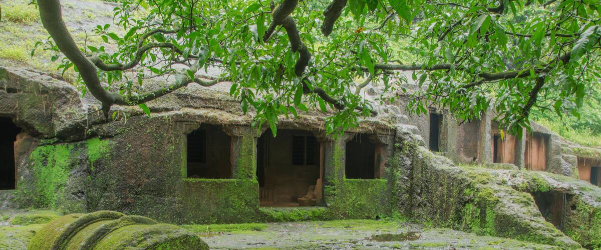 A moss-covered ancient structure with thatched-roof huts and large moss-covered boulders.