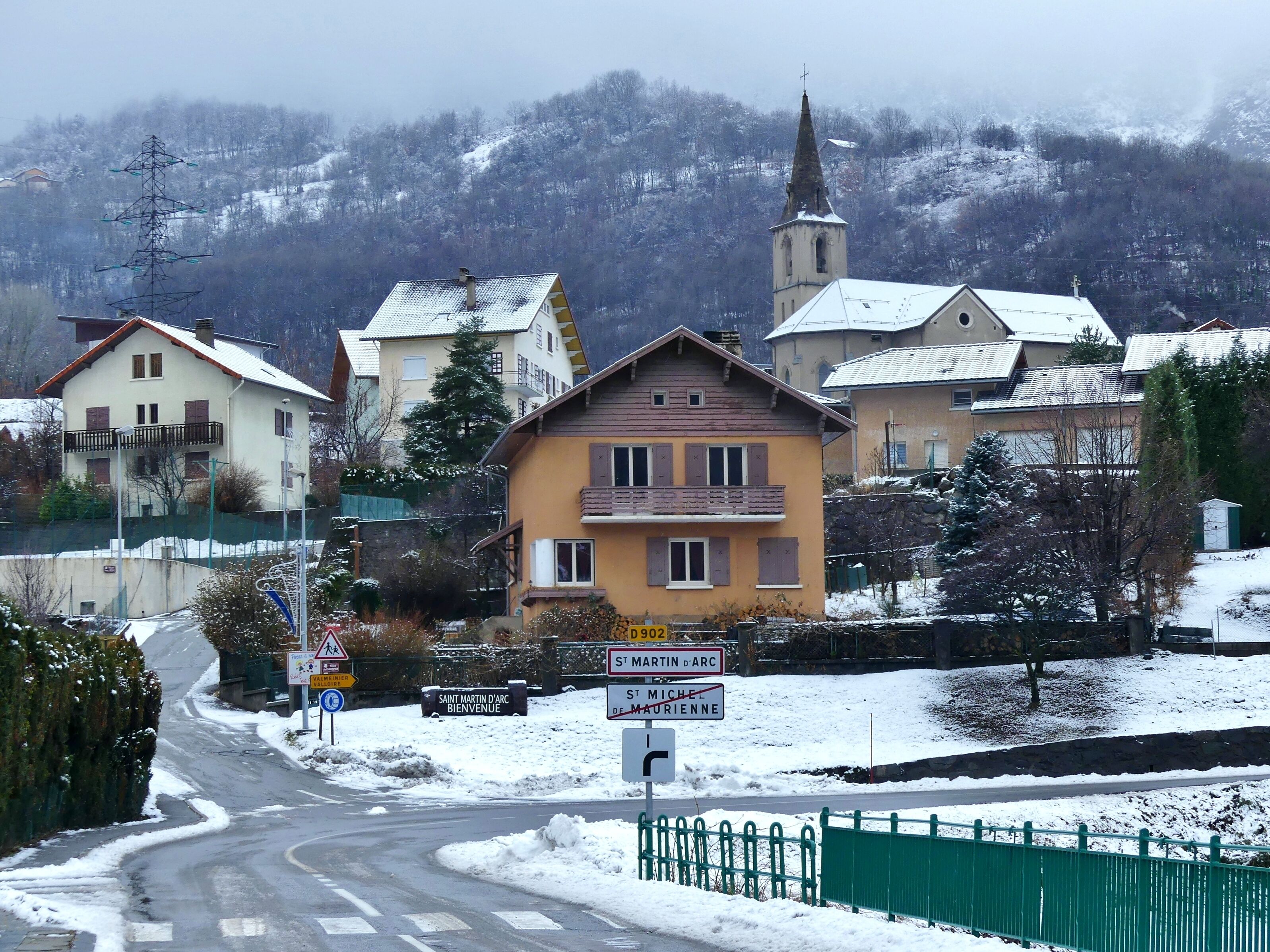 A snow-covered village with houses, a church, and a sign indicating 'Saint Martin d'Arc'.