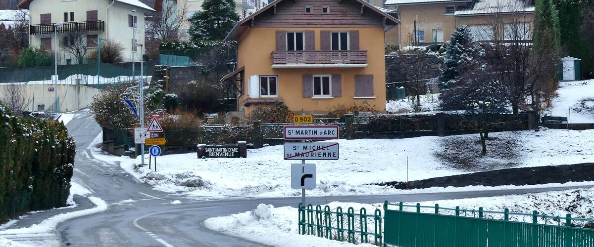 A snow-covered village with houses, a church, and a sign indicating 'Saint Martin d'Arc'.