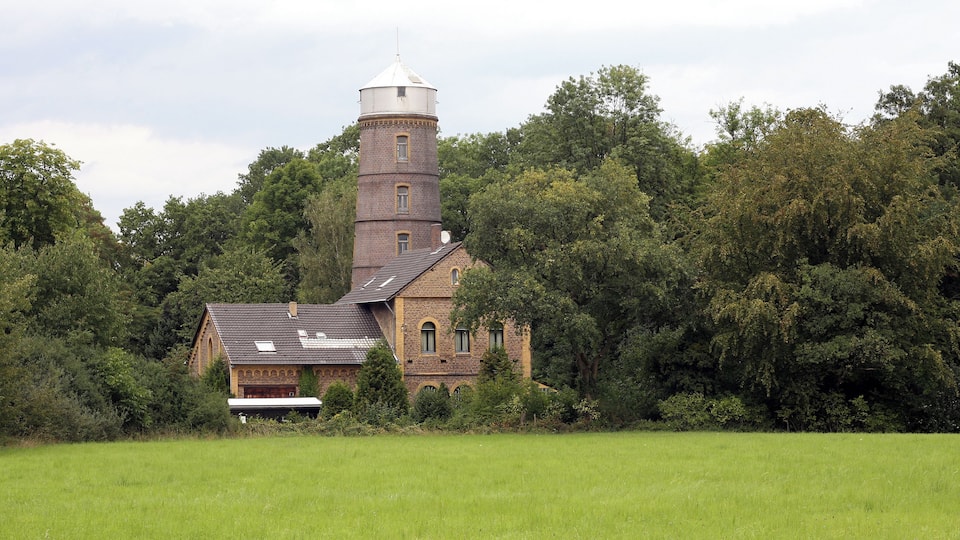 A historic brick building with a tower and a field in the foreground.