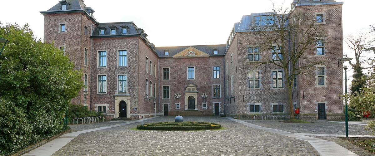 A historic building with a courtyard, cobblestone path, and a central spherical sculpture.