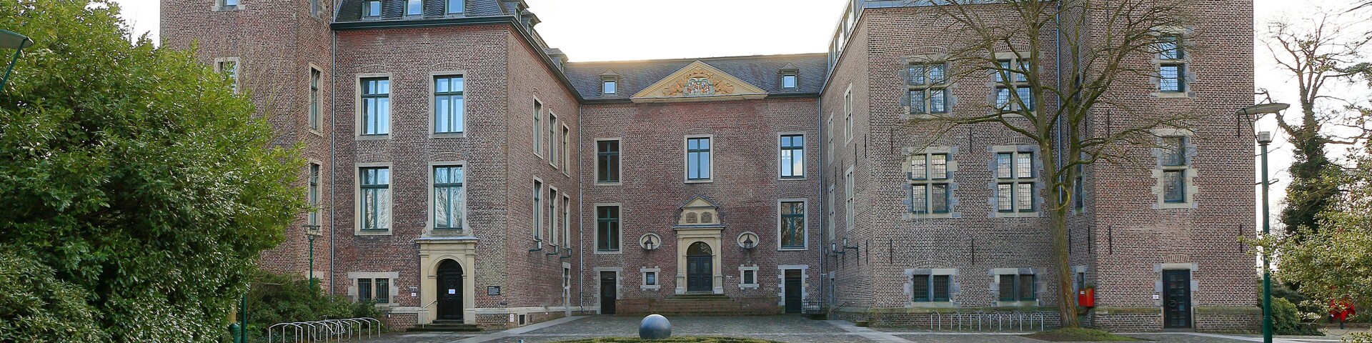A historic building with a courtyard, cobblestone path, and a central spherical sculpture.