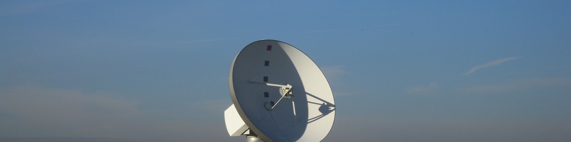 A large satellite dish in a field with a church and houses in the background.