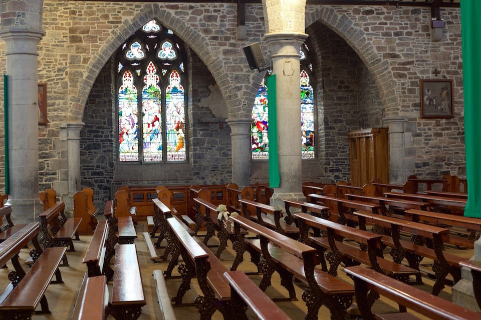A church interior with stone walls, wooden pews, and stained glass windows.