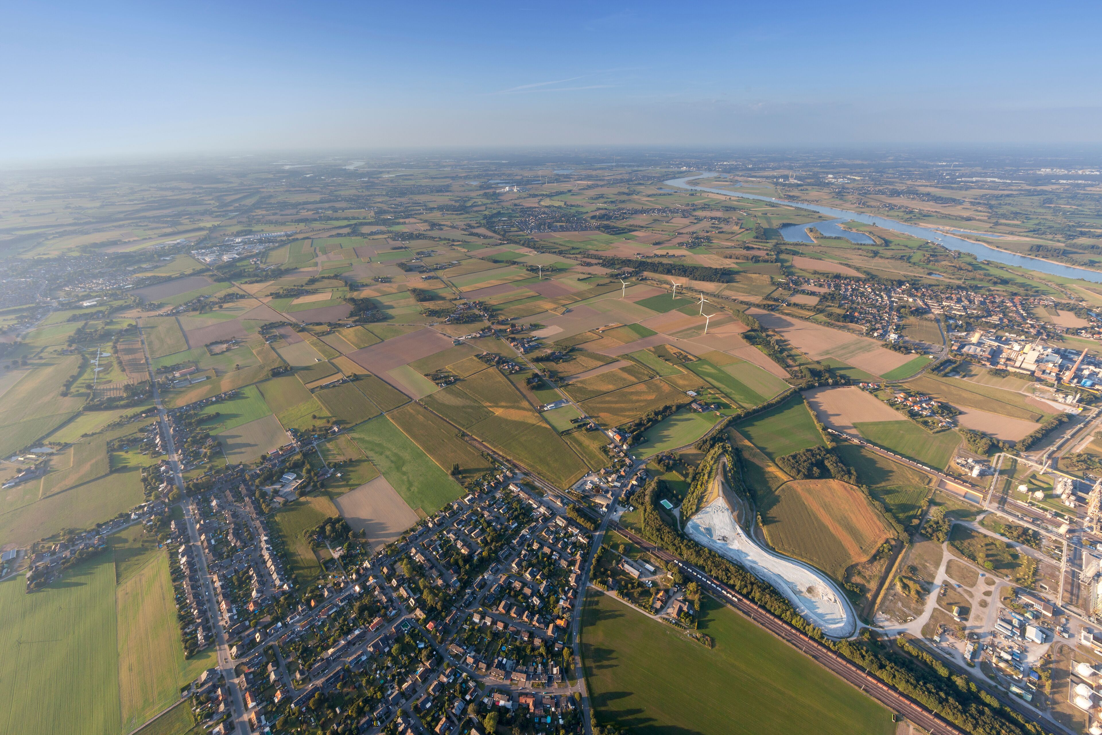 An aerial view of a rural landscape with fields, a winding river, and a small town with a bridge.