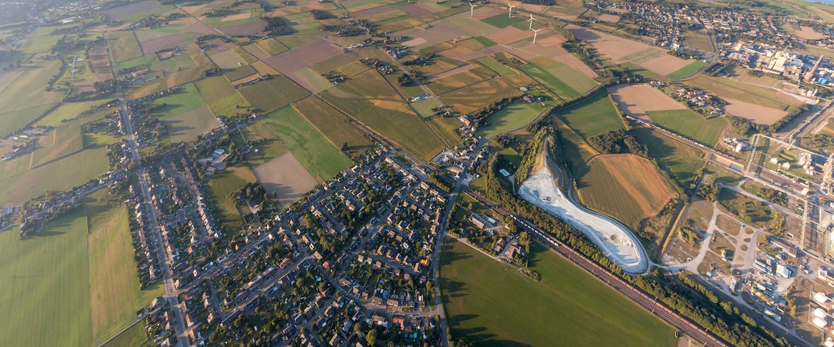 An aerial view of a rural landscape with fields, a winding river, and a small town with a bridge.