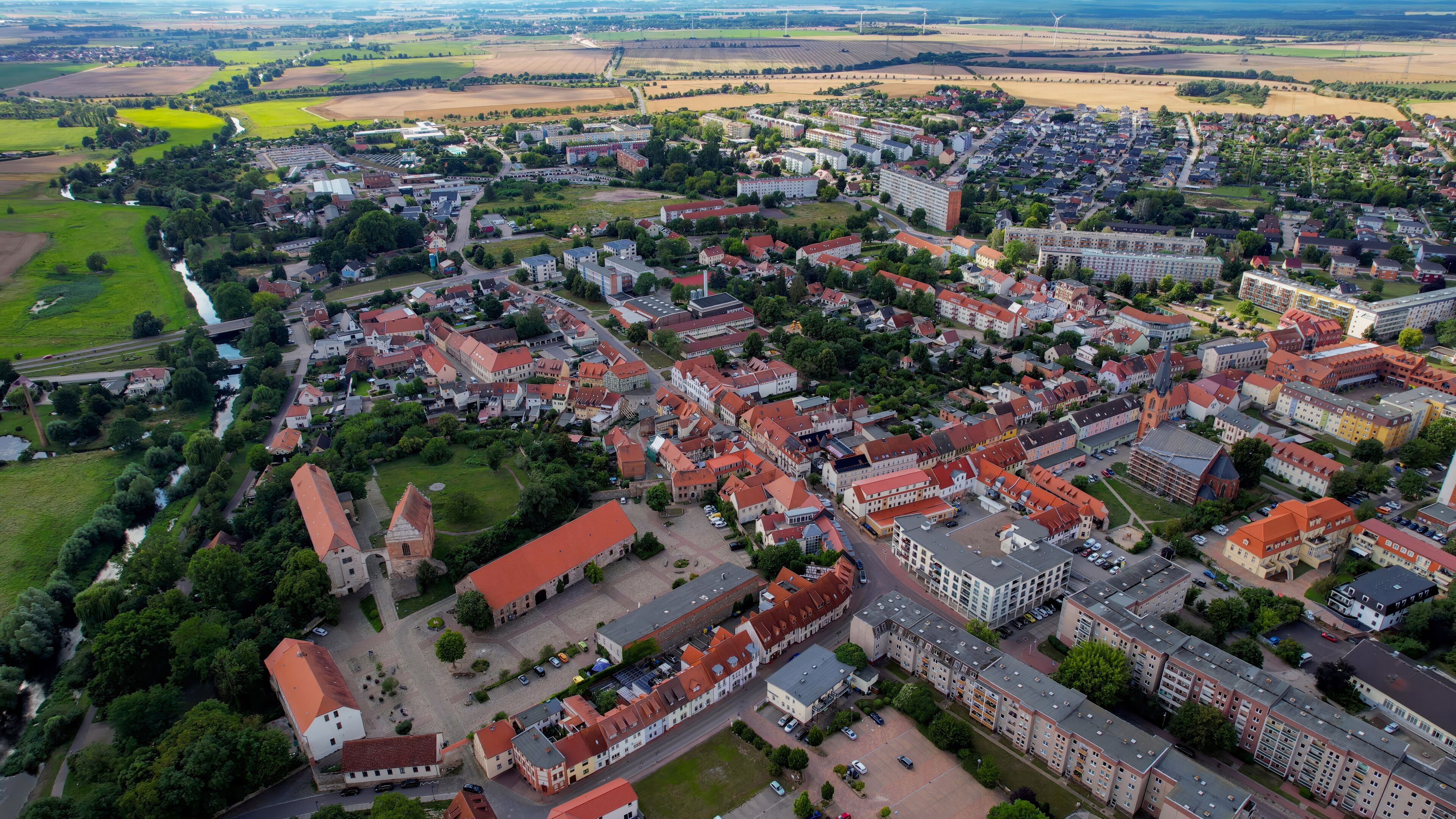 An aerial view of a town with red-roofed buildings, green fields, and a river.