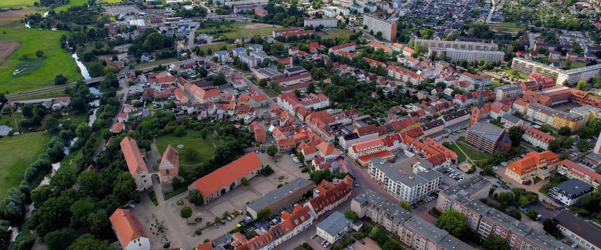 An aerial view of a town with red-roofed buildings, green fields, and a river.
