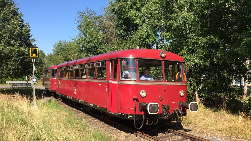 A red vintage train on tracks surrounded by greenery.
