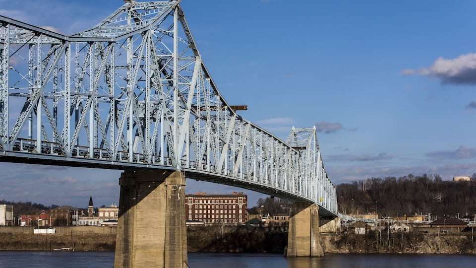 A large steel bridge spanning a river with a town in the background.