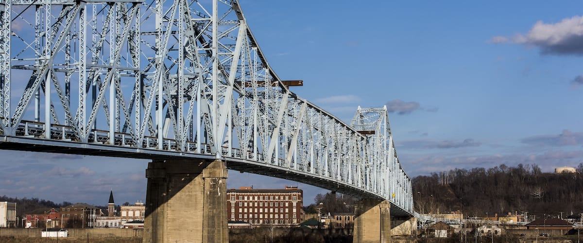 A large steel bridge spanning a river with a town in the background.