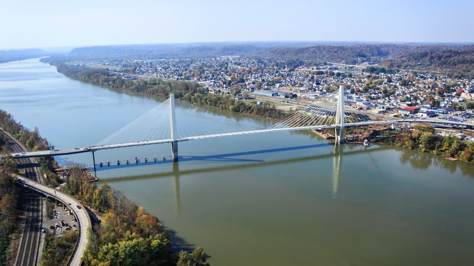 A suspension bridge over a river, surrounded by a town and forested hills.