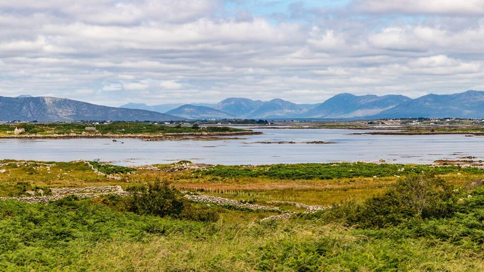 A coastal landscape with mountains in the background, a body of water, and green vegetation in the foreground.