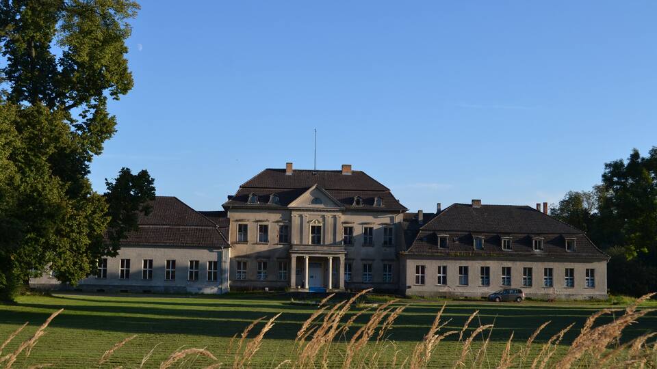 A large, stately building with a symmetrical facade, surrounded by lush green fields and tall grasses.