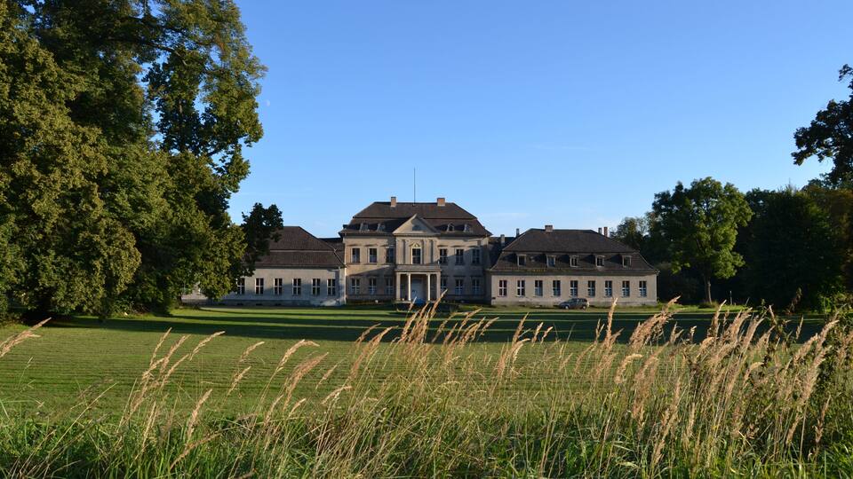 A large stately house with a symmetrical facade, surrounded by lush greenery and a well-maintained lawn.
