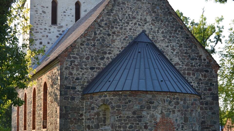 A stone church with a bell tower and a conical roof.