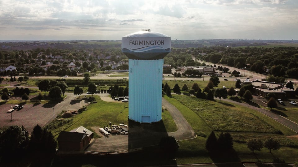 A large water tower labeled 'Farmington' surrounded by a green landscape with trees and a road.