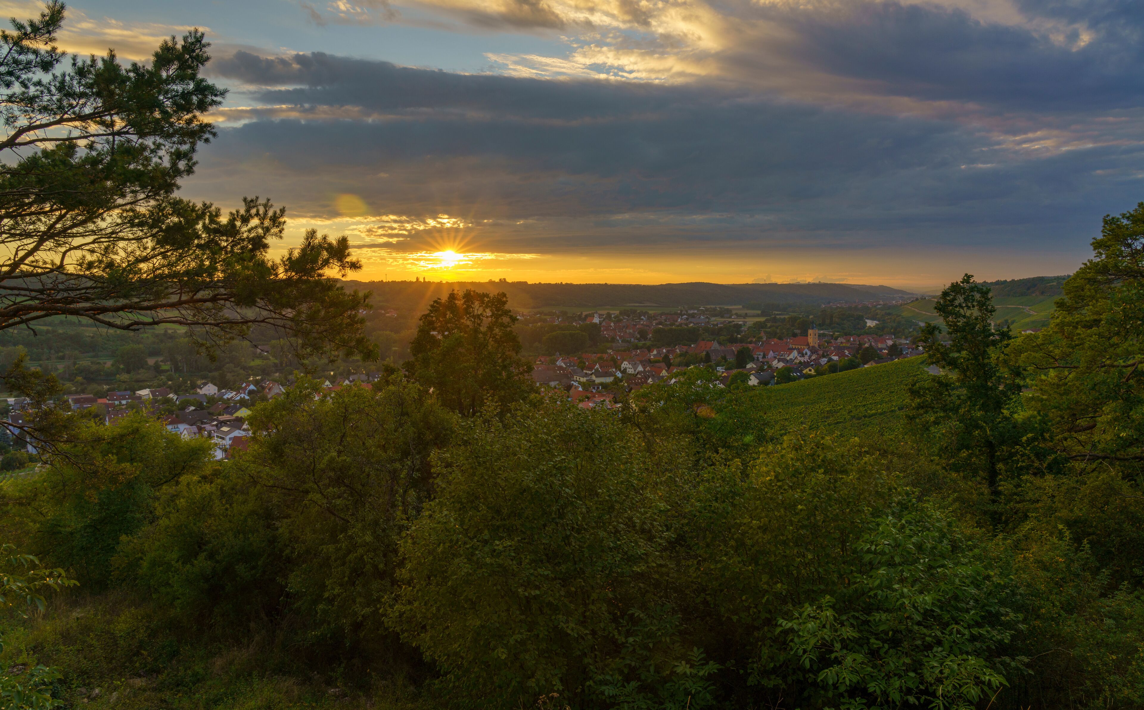 A sunset over a town surrounded by hills and trees.