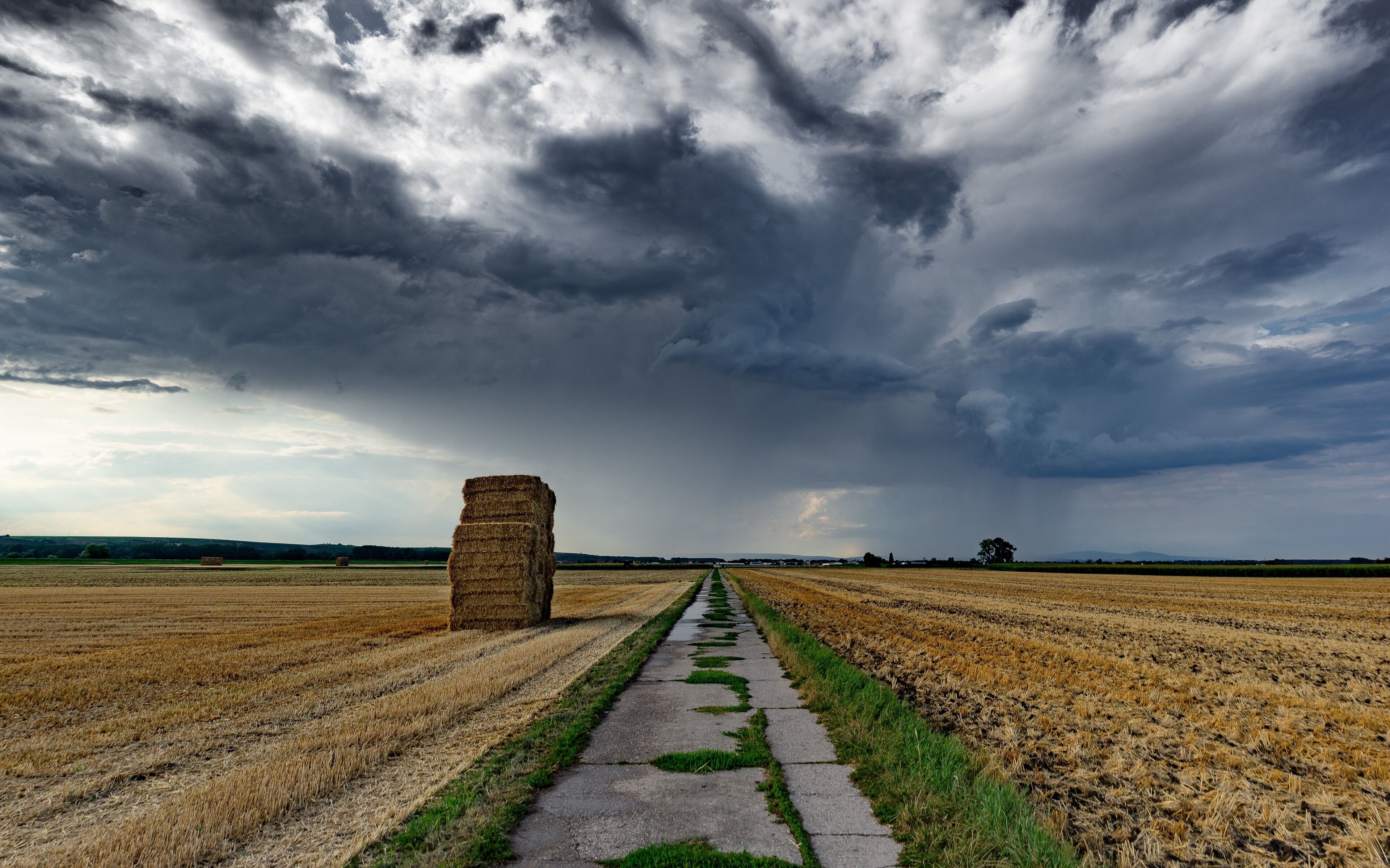 A rural landscape with a path leading to a haystack under a stormy sky.