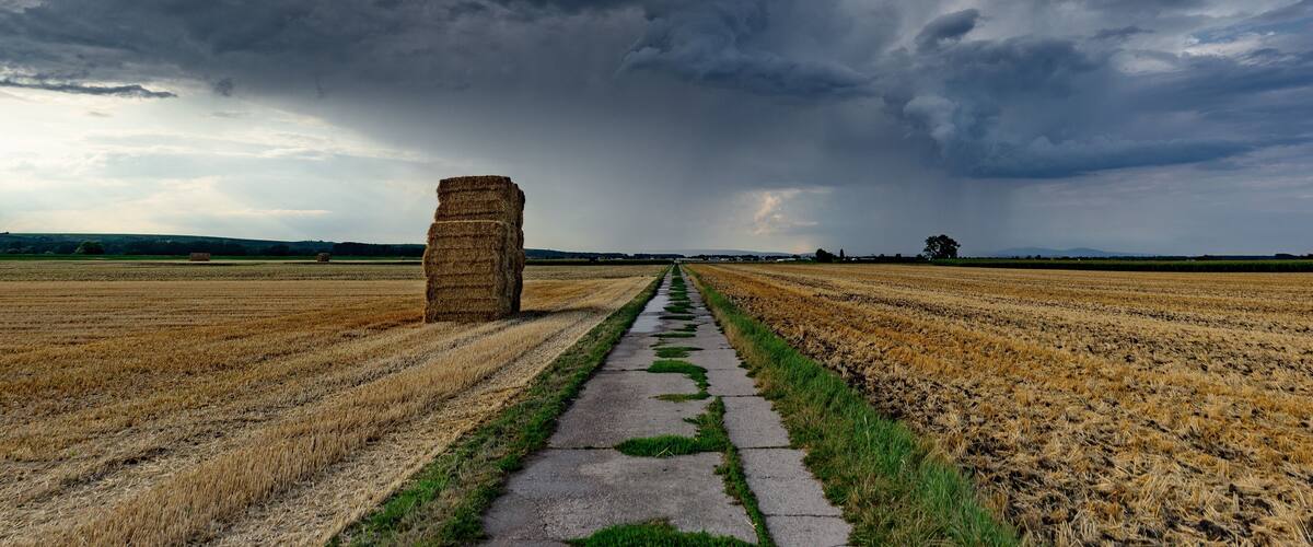 A rural landscape with a path leading to a haystack under a stormy sky.