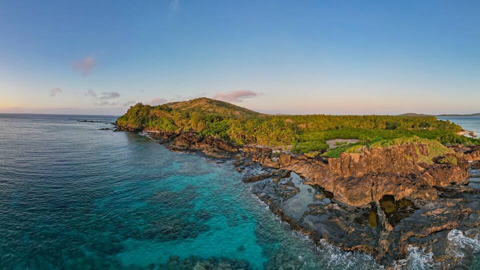 A coastal landscape with clear turquoise waters, rocky cliffs, and lush greenery.