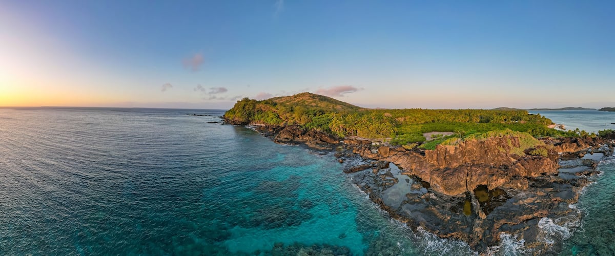 A coastal landscape with clear turquoise waters, rocky cliffs, and lush greenery.