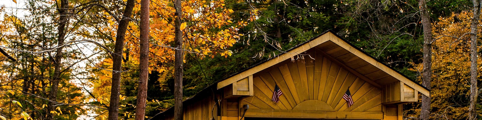A wooden covered bridge with an American flag, surrounded by autumn foliage.