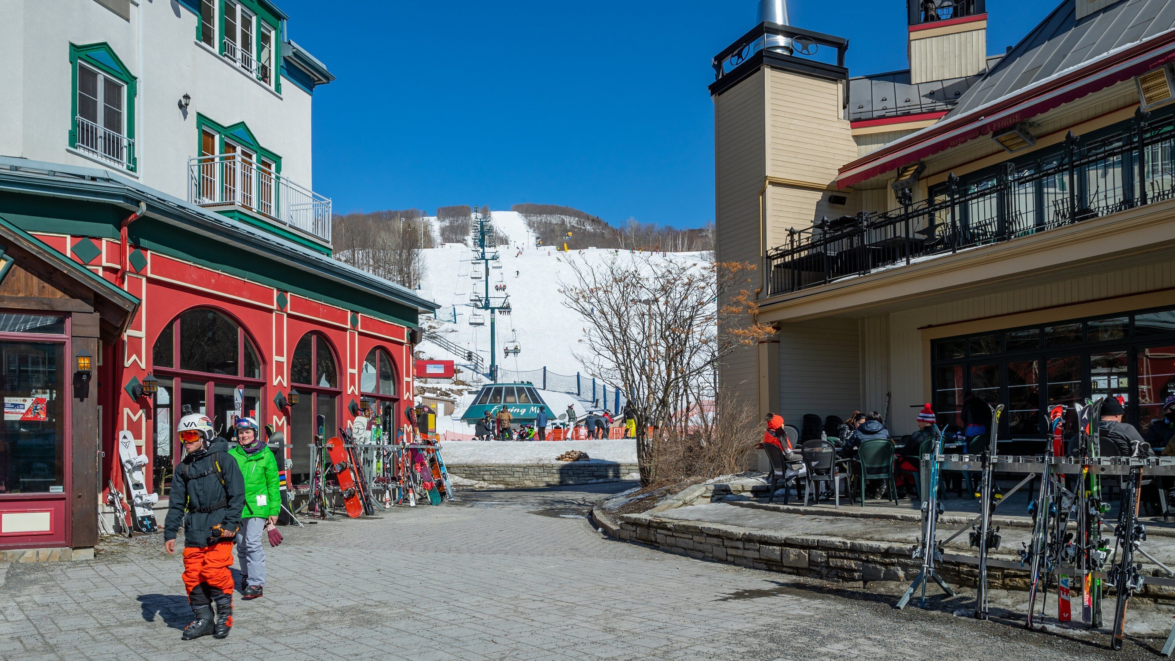 Une pente de montagne enneigée avec un télésiège, un bâtiment rouge avec un auvent vert et un café doté d’une terrasse.