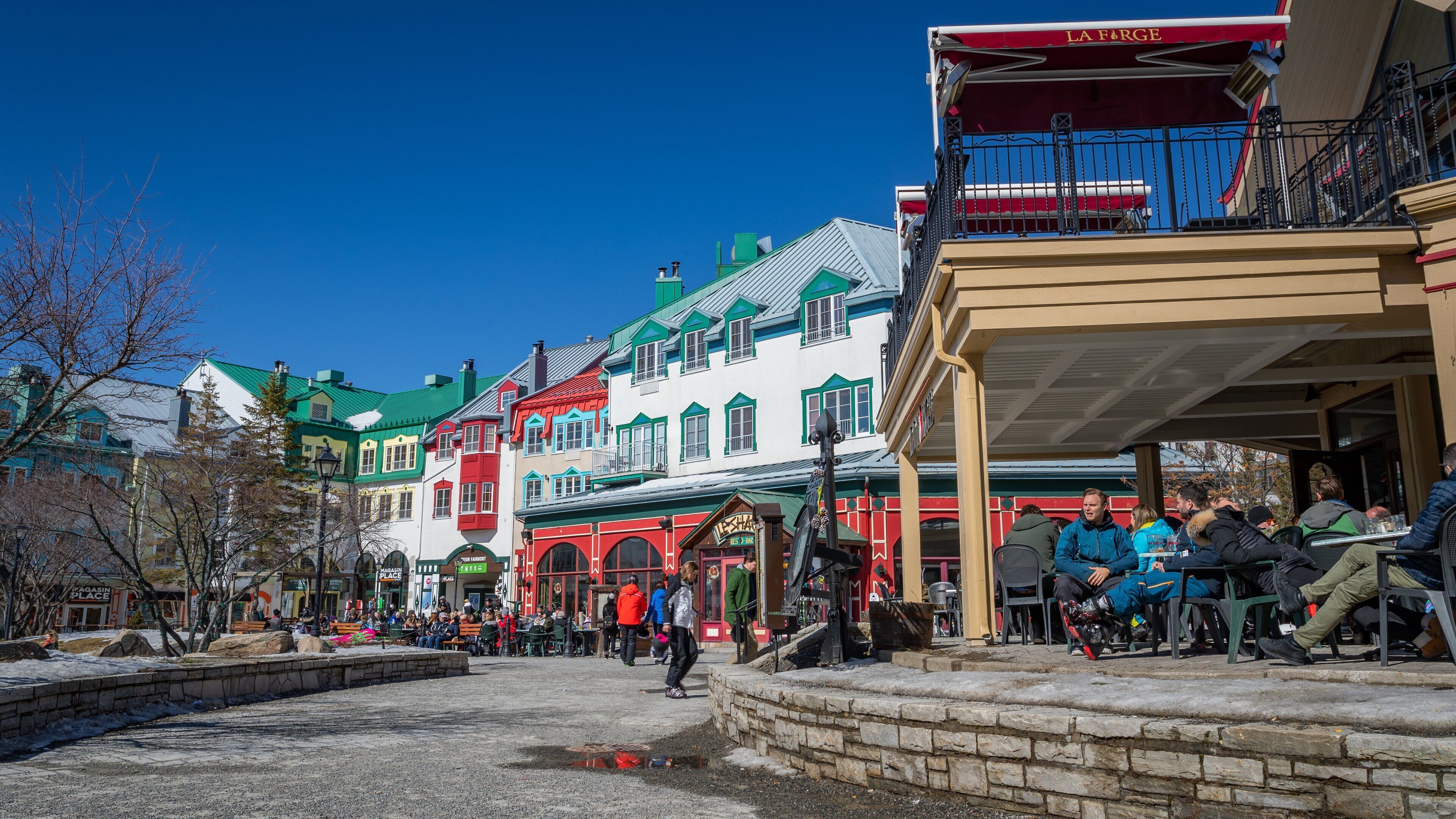 A colorful street with buildings, a stone wall, and people sitting at outdoor tables.