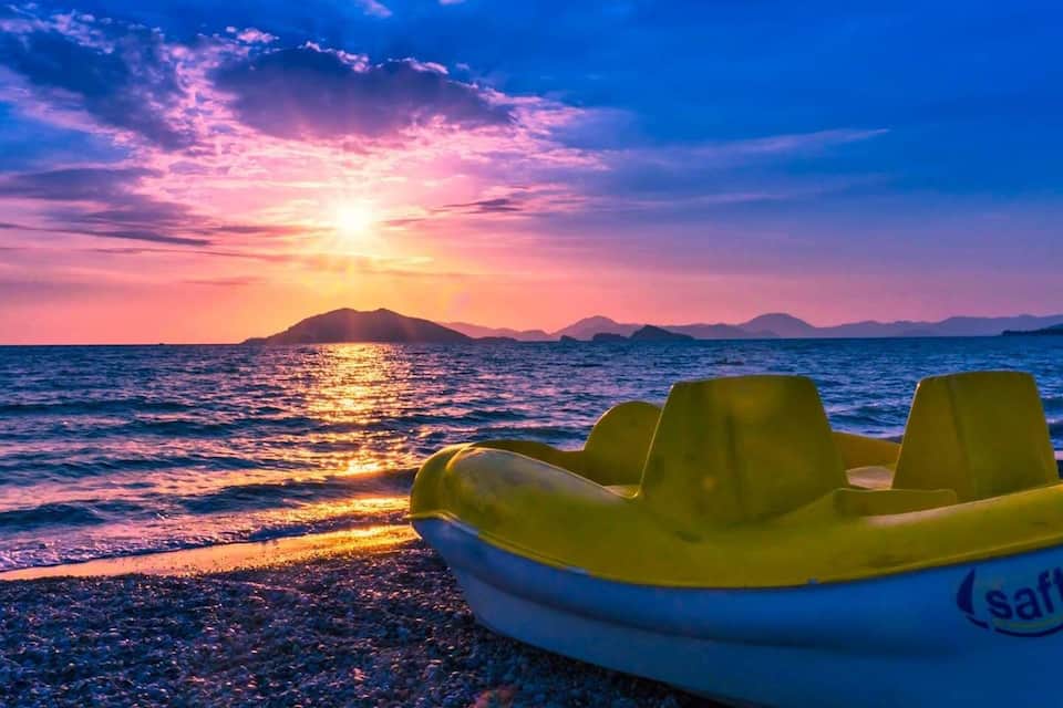 A boat on a rocky shore with a sunset over the ocean and mountains in the background.