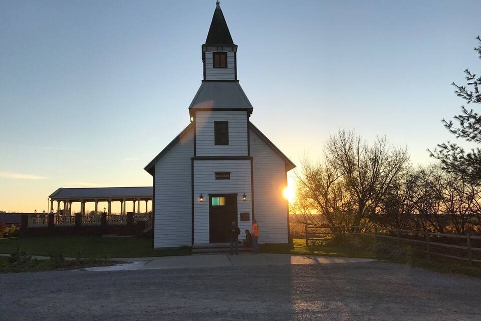 A white church with a steeple and a sign reading "ME CHURCH" at sunset.