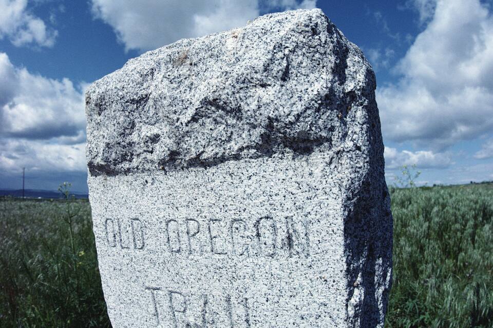 Un hito de piedra con inscripciones, frente a un cielo despejado y un campo cubierto de hierba.