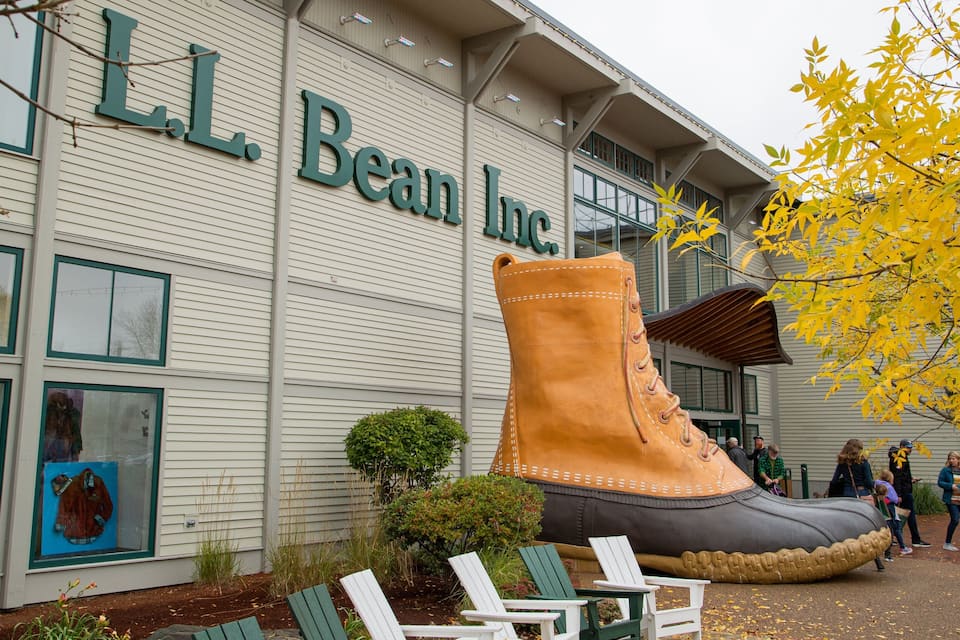 Un edificio con el rótulo 'L.L. Bean Inc.', una gran escultura de una bota y mesas al aire libre.